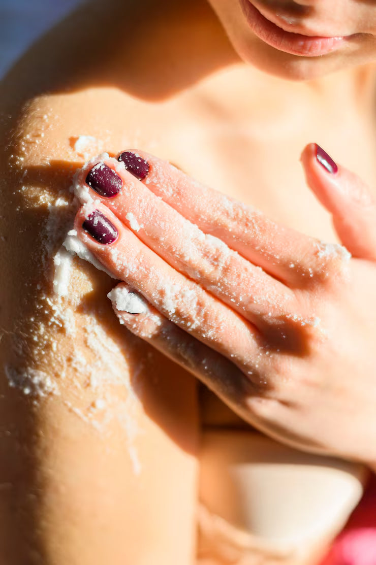 Woman applying homemade body scrub to her shoulder, exfoliating skin with natural ingredients.