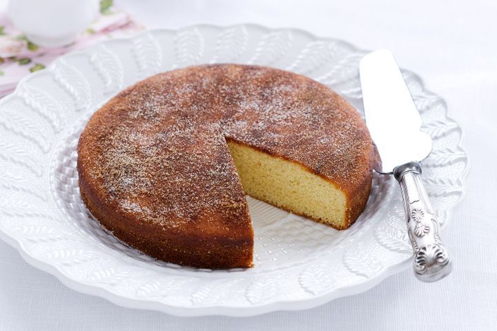 Round cinnamon teacake with a slice cut out, served on a white plate with a cake knife.